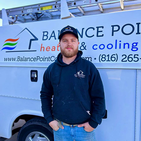 Chris standing with his hands in his pockets in front of the Balance Point work truck. He is wearing a navy sweatshirt with the Balance Point logo and a baseball cap.