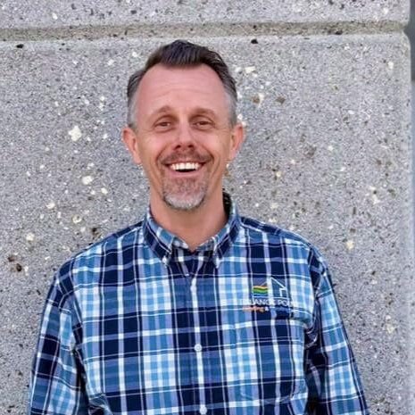 Justin wearing a blue flannel shirt standing in front of a gray wall